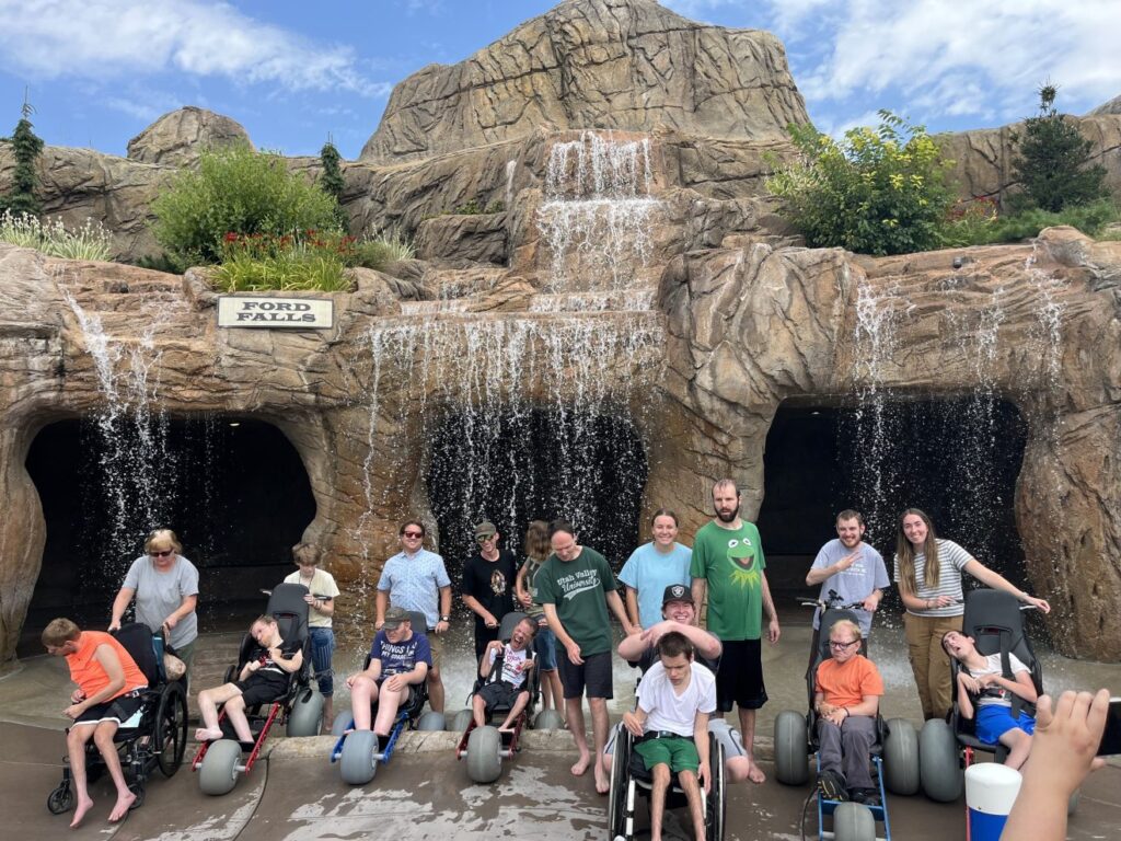 group of friend pose in front of a waterfall. Some of them are wheelchair users in the extreme motus all terrain wheelchair